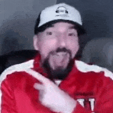 a man with a beard is wearing a red jacket and a white hat and pointing at something .