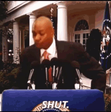 a man in a suit and tie stands at a podium with the word shut on it