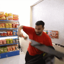a man in a red shirt is holding a sword in front of a shelf of potato chips