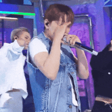 a man in a denim vest is singing into a microphone on a stage
