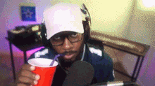 a man wearing headphones and a nike hat is drinking from a red cup