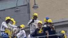 a group of people wearing yellow hats and scarves are standing on a balcony .