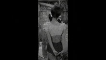 a black and white photo of a woman in a swimsuit standing in front of a bamboo wall .