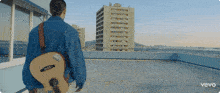 a man is holding a guitar on a rooftop with the word vevo on the bottom