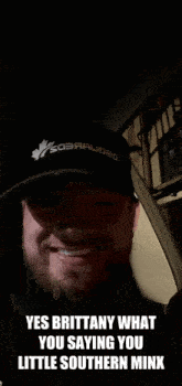 a man with a beard wearing a black hat with the words yes brittany what you saying you little southern minx on the bottom