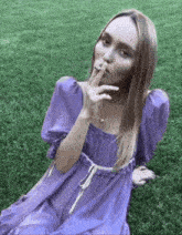 a woman in a purple dress is smoking a cigarette in the grass .