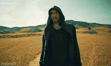 a man with a hood is standing in a field .
