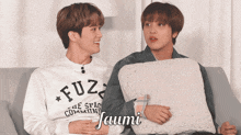 two young men are sitting on a couch and one has a sweatshirt that says fuz on it