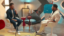 a man in a suit is sitting in a chair talking to another man