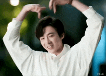 a young man is making a heart shape with his hands while wearing a white shirt .