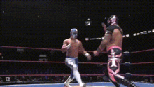 a wrestler is laying on the ground in a boxing ring while a referee watches .