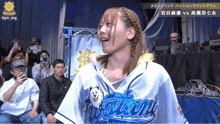 a woman wearing a blue and white hawaii shirt stands in front of a crowd