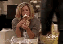 a woman is sitting at a table eating a donut with soapnet.com written on the bottom