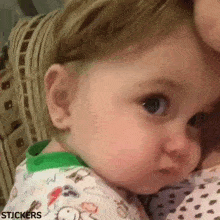 a baby is being held in a woman 's arms and looking at the camera .