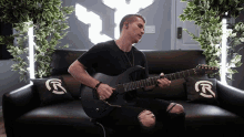 a man sits on a couch playing a guitar with a yamaha logo on the pillow