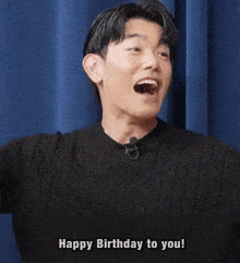 a man in a black sweater is laughing and saying happy birthday to you .