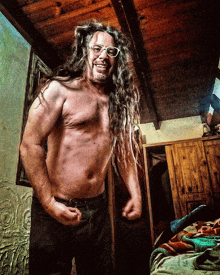 a shirtless man with long dreadlocks and glasses stands in a room