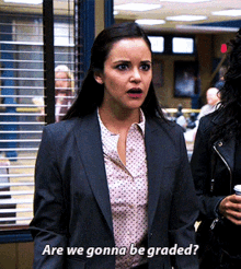 a woman in a suit and polka dot shirt is asking if we gonna be graded