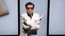 a man in a white suit and red heart shaped glasses