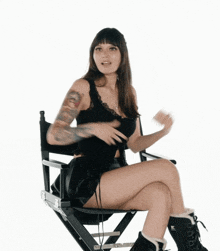 a woman is sitting in a director 's chair with her legs crossed and a tattoo on her arm .