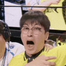 a man wearing glasses and a yellow shirt is making a funny face while sitting in a stadium .