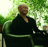 a bald man is sitting in a green chair with trees in the background