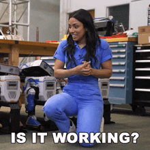 a woman in blue scrubs is kneeling down in front of a robot and the question is " is it working "