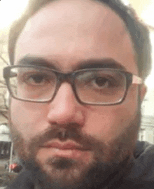 a man with a beard and glasses is looking at the camera .