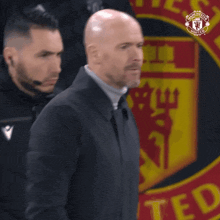 a man in a suit is standing in front of a manchester united logo