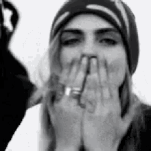 a black and white photo of a woman wearing a beanie and covering her mouth with her hands .