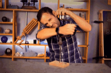 a man in a plaid shirt is hammering a nail into a wooden box