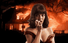 a woman in front of a burning house smoking a cigarette