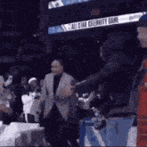 a man in a suit is shaking hands with another man in front of a sign that says all star celebrity game .