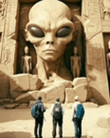 three people are standing in front of a large statue of an alien .