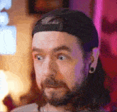a man with a beard and long hair is wearing a black hat and ear plugs .