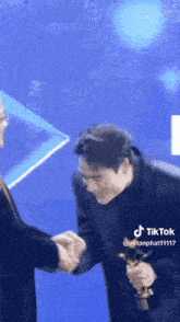a man in a suit and tie is shaking hands with another man holding a trophy .