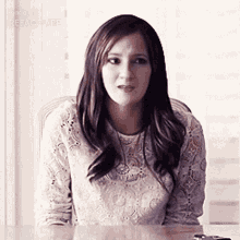 a woman in a white lace top is sitting at a table and making a face .
