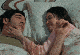 a man and a woman are laying on a bed and the woman is touching the man 's face