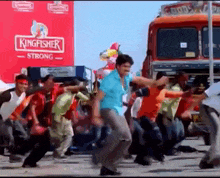 a group of men are dancing in front of a kingfisher strong truck