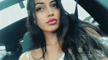 a woman with long hair is sitting in a car and taking a selfie with her phone .