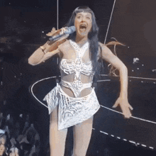 a woman is singing into a microphone on a stage while wearing a white dress .