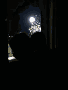 a couple looking out a window at fireworks at night