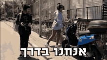 two people walking down a sidewalk with a blue scooter in the foreground