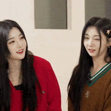 two girls are sitting next to each other with one wearing a brown sweater with the letter r on the front