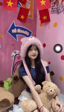 a girl in a pink hat holds a teddy bear in front of a sign that says check it out