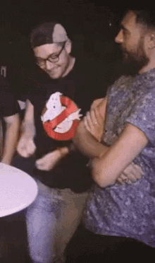 a man wearing a ghostbusters shirt stands next to another man with his arms crossed