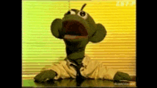 a green puppet is sitting at a desk with its mouth wide open
