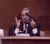 a man in a suit and tie is holding a gun while giving a speech in front of a microphone .