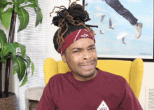 a man wearing a maroon vans shirt is sitting in a chair