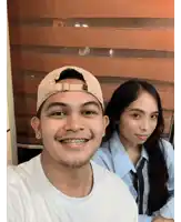 a man wearing a hat and braces smiles next to a woman